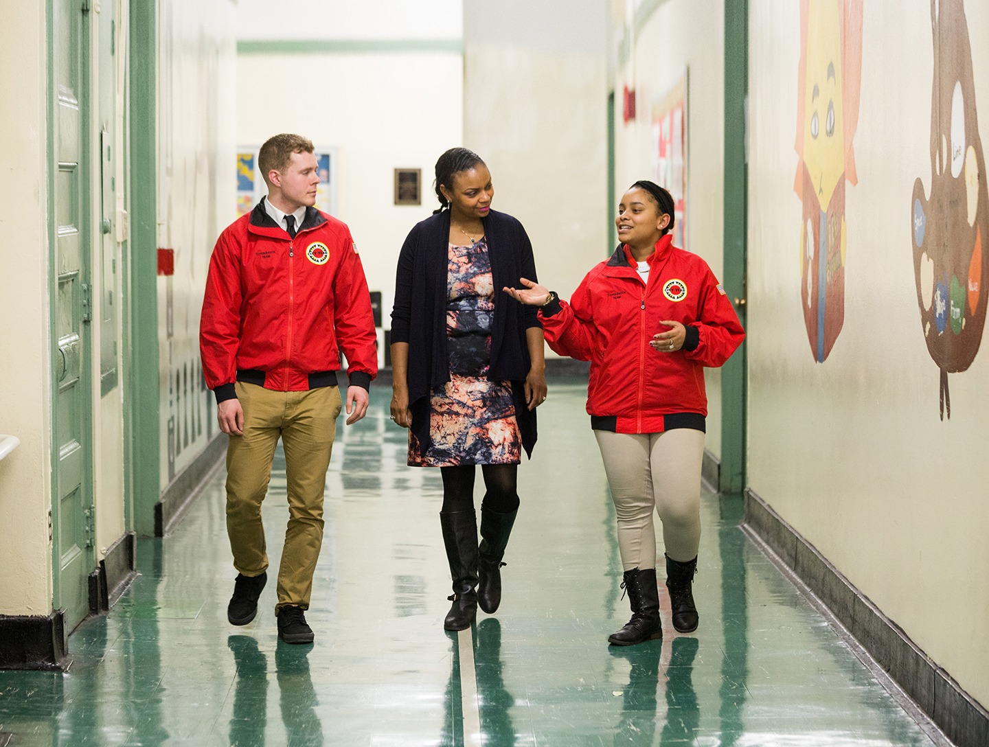 Two AmeriCorps members walking and talking with a ɫƵ team supporter in a school hallway