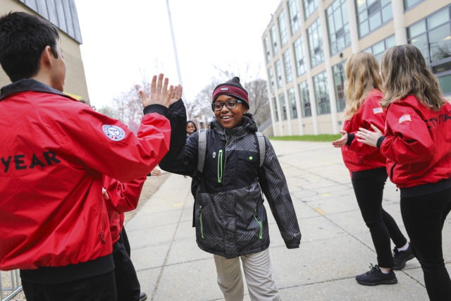 An elementary school student wearing glasses high fives a ɫƵ AmeriCorps member outside their school