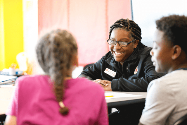 A ɫƵ Buffalo AmeriCorps member laughs and looks across the table at two students